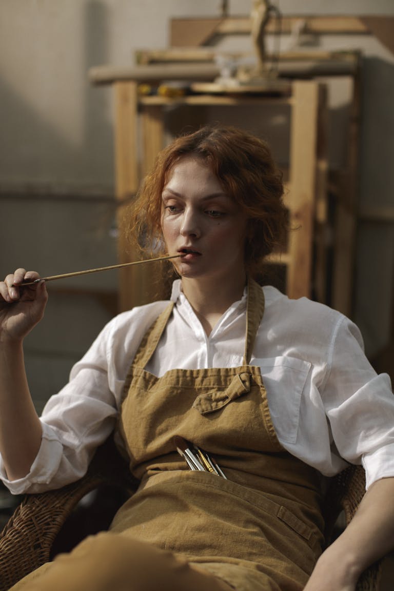 Artist seated in a studio holding a paintbrush, deep in thought. Perfect for creative inspiration themes.