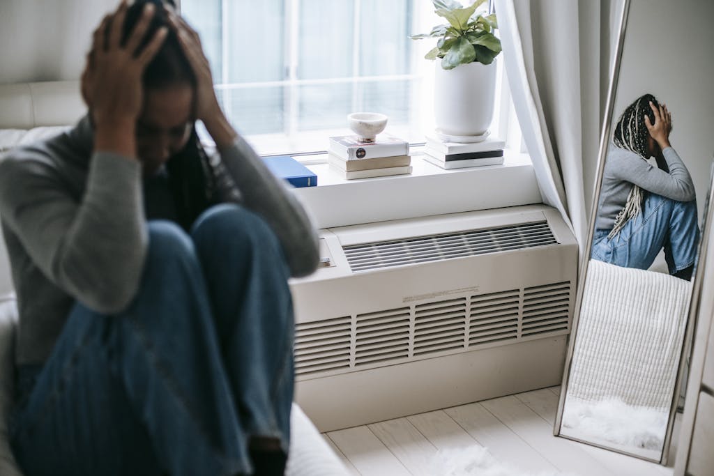 Frustrated young female having mental problem reflecting in mirror while sitting alone in room