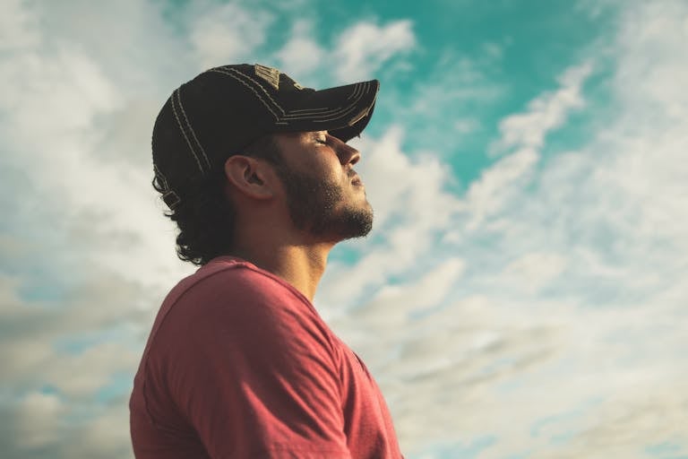 A man enjoys outdoor relaxation and mindfulness beneath a bright, cloudy sky, exuding calm and peace.