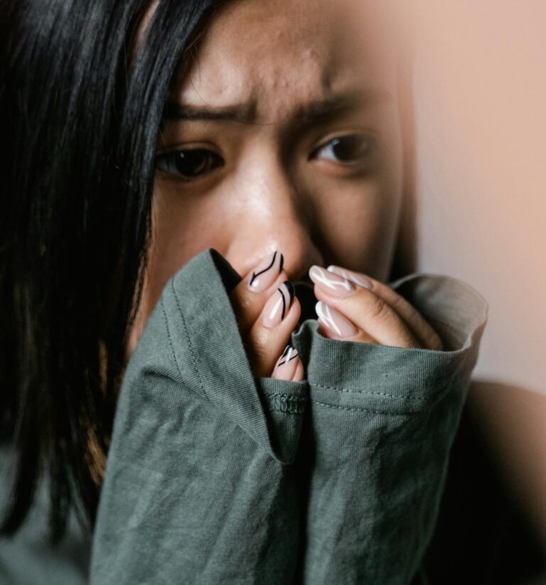 A woman appears anxious, covering her mouth with a green sweater sleeve in a close-up shot.