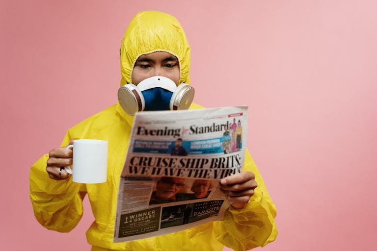 Person in yellow protective suit reading a newspaper with a mug.