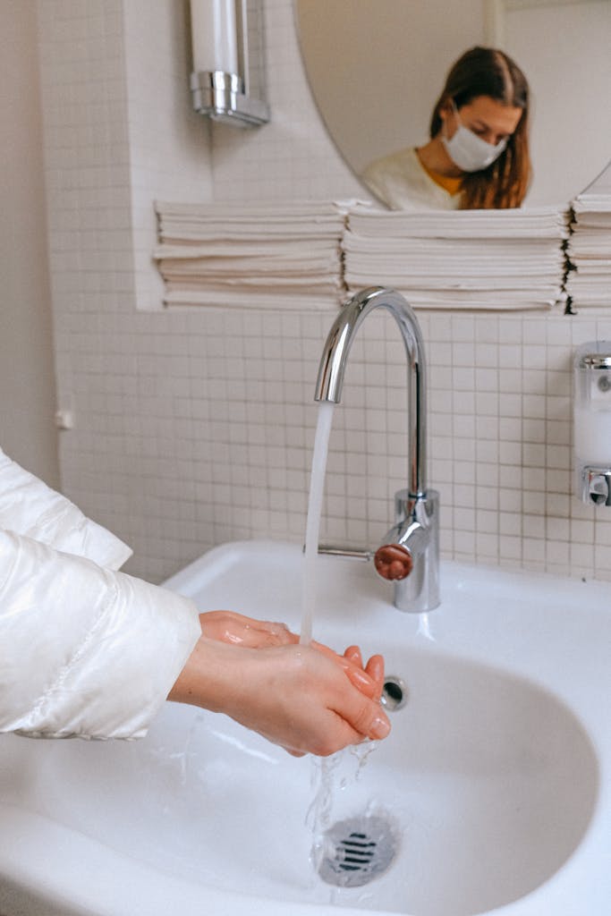 Woman wearing a face mask washing hands in a clean bathroom with a focus on hygiene and health.