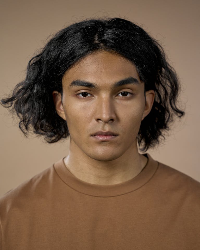 Studio portrait of a young man with medium-length hair and neutral expression.